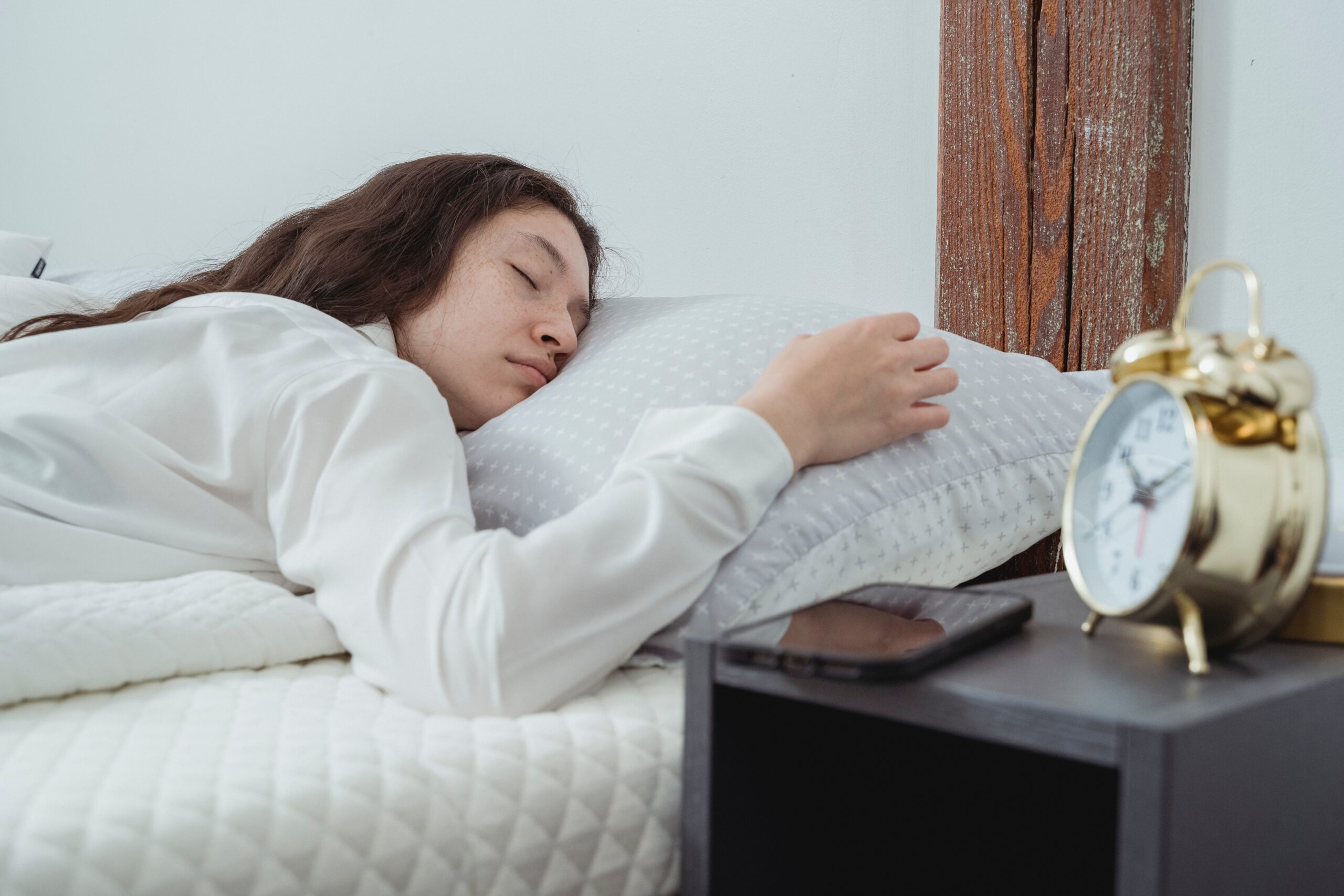 A sleeping woman in bed next to her phone on her nightstand