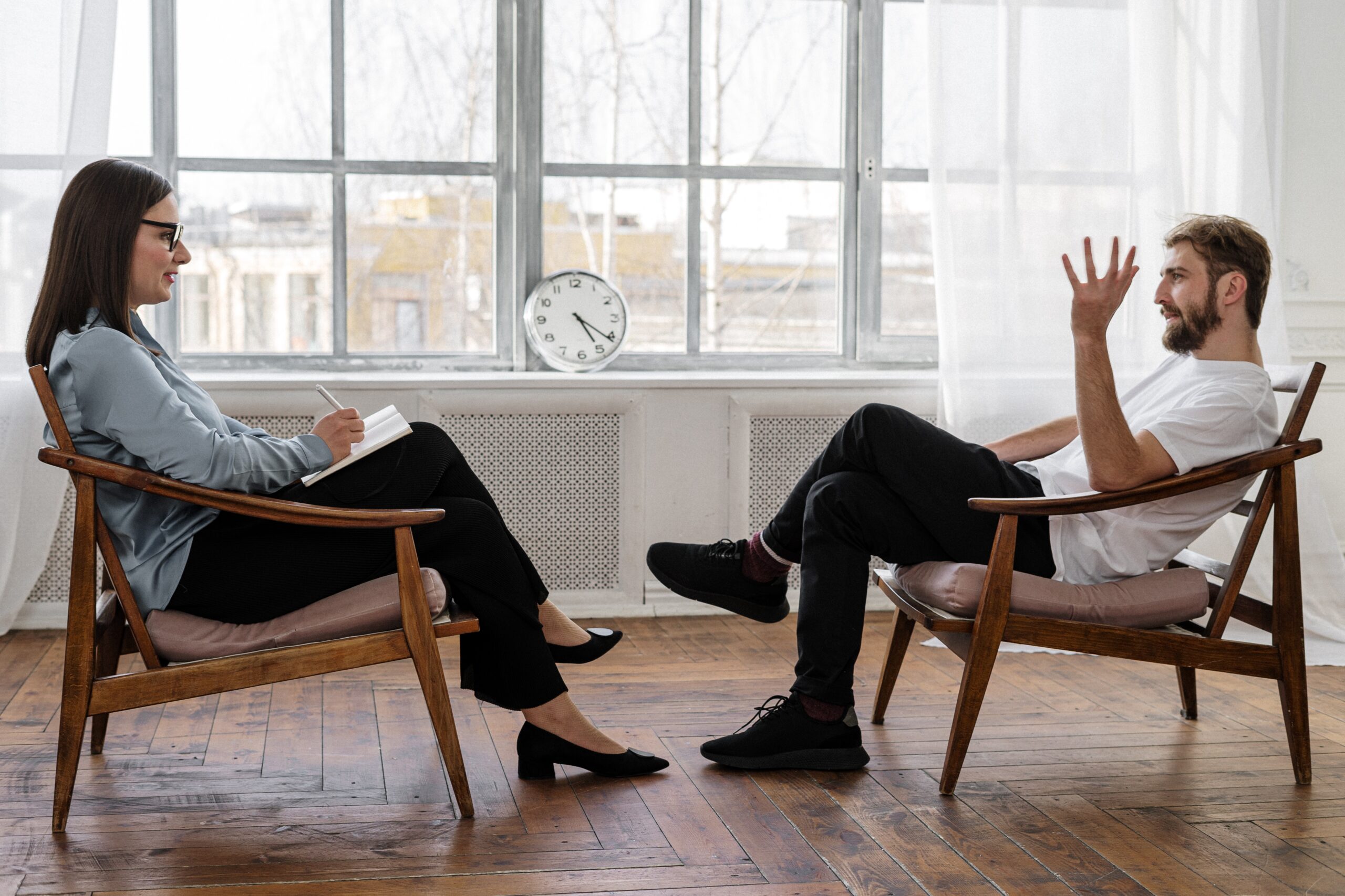 A man sitting right across his therapist in a mostly empty room with an old wooden floor.