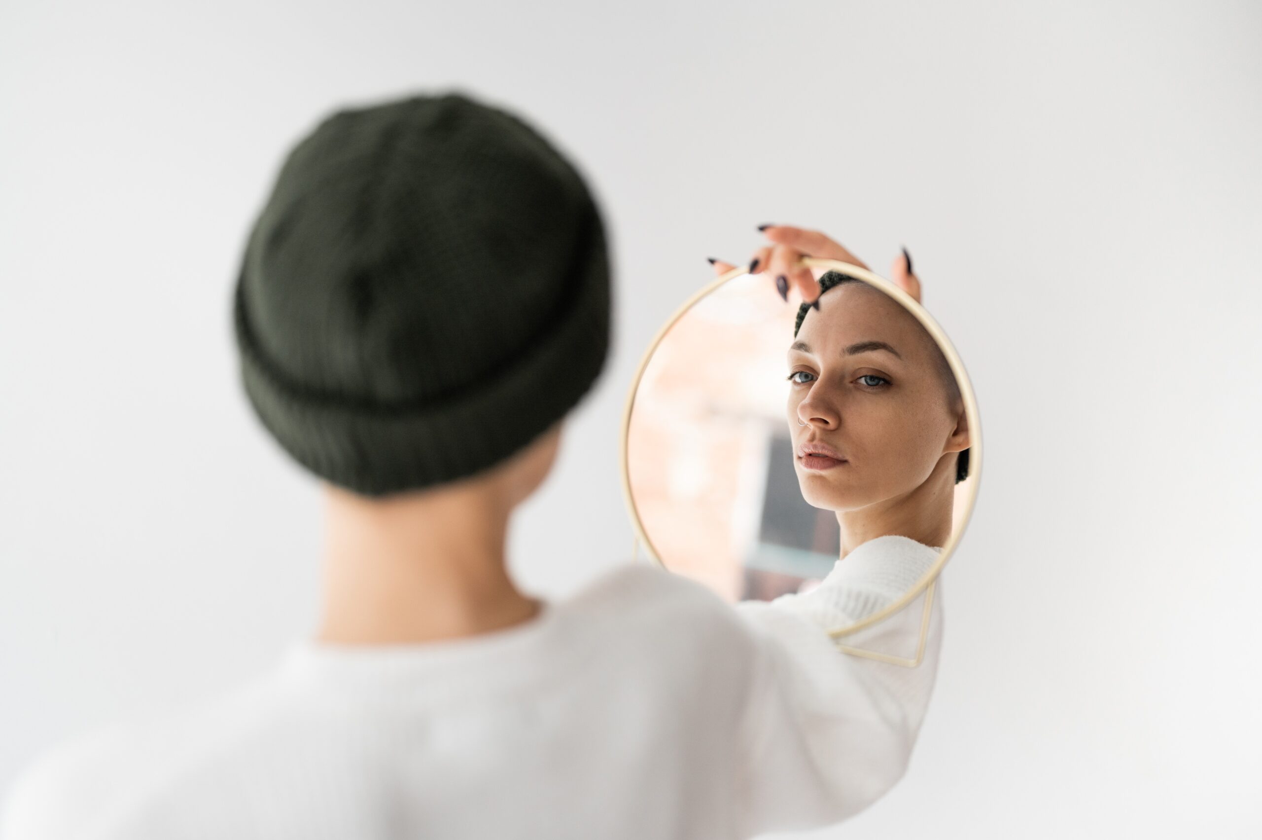 A woman looking at herself in the a round mirror she is holding up herself.